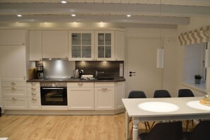 A modern kitchen with white cabinetry, a built-in oven, and a dining area with a white table and chairs. - 1 Aruba at Haus Boldix (Wyk-Boldixum)