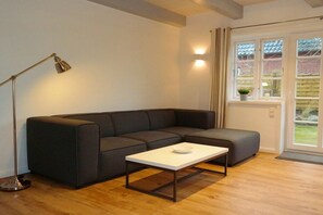 A modern living room with a sectional sofa, a coffee table, a floor lamp, and a window with curtains. - 4 Caymans at Boldix House (Wyk-Boldixum)