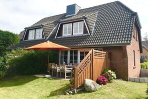 A two-story house with a sloped roof, a covered patio with outdoor furniture, and a brick exterior. - View of the dike in Nieblum (Nieblum)