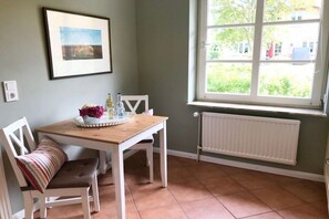 A dining area with a table, chairs, a window with a view, and a radiator. - View of the dike in Nieblum (Nieblum)