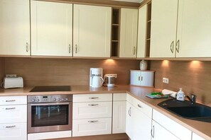 A modern kitchen with white cabinets, a built-in oven, a coffee maker, and a sink. - View of the dike in Nieblum (Nieblum)