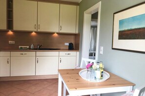 A kitchen with white cabinets, a wooden table with a tray, and a framed picture on the wall. - View of the dike in Nieblum (Nieblum)