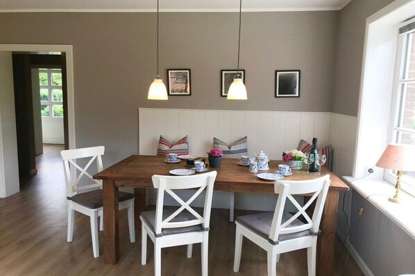 A dining area with a wooden table, white chairs, and pendant lighting. - View of the dike in Nieblum (Nieblum)