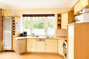 A kitchen with wooden cabinets, a dishwasher, a stove, and a window with a view of greenery. - Beach blossom in Margarethenhof (Wyk auf Föhr)