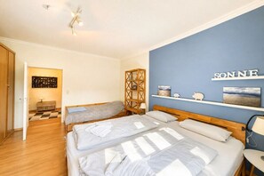 A hotel room with two beds, a wooden wardrobe, a small table, and a shelf with decorative items. - Beach blossom in Margarethenhof (Wyk auf Föhr)