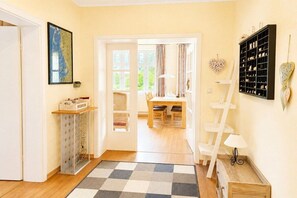 Ein Zimmer mit einem Schachbrettmuster-Teppich, einer weißen Tür, die in einen Essbereich führt, einer Leiter und einem Regal mit Dekorationsobjekten.