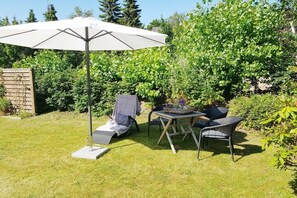 Ein Außenbereich zum Sitzen mit Tisch und Stühlen, einem großen Sonnenschirm und einer Liege.