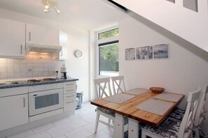A modern kitchen with white cabinets, a wooden dining table, and a window providing natural light. - Waldstrasse - Holiday Apartment 26 (Wyk auf Föhr)