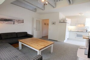 Ein modernes Wohnzimmer mit einer Couch, einem Holztisch und einer Küche im Hintergrund.