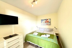 A hotel room with a bed, a flat-screen TV mounted on the wall, a bedside table, and a painting on the wall. - Uthlande Holiday Apartment 14 (Wyk auf Föhr)