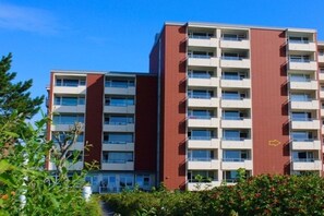 A multi-story residential building with a red and white facade, balconies, and a clear sky. - Uthlande Holiday Apartment 14 (Wyk auf Föhr)