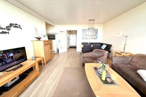 A modern living room with a flat-screen TV, wooden furniture, a brown sofa, and a coffee table with decorative items. - Uthlande Holiday Apartment 14 (Wyk auf Föhr)