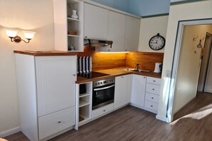 A compact kitchen with white cabinetry, a wooden countertop, a built-in oven, and a wall-mounted clock. - Otto House - Holiday Apartment 1 (Wyk auf Föhr)