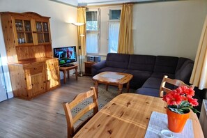 Ein Wohnzimmer mit einer Couch, einem Holzessttisch, Stühlen, einem Fernseher und einem Schrank.