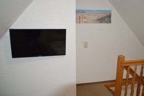 A room with a mounted television on the wall, a painting of a beach scene, and a wooden staircase. - Hüs am a Süüd Ferienwohnung Ley (Dunsum)