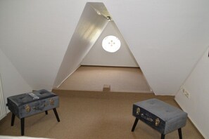 A room with a sloped ceiling, two small tables with drawers, and a light fixture. - Hüs am a Süüd Ferienwohnung Ley (Dunsum)