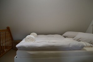 A neatly made bed with striped bedding and rolled towels, a wooden chair, and a plain wall. - Hüs am a Süüd Ferienwohnung Ley (Dunsum)