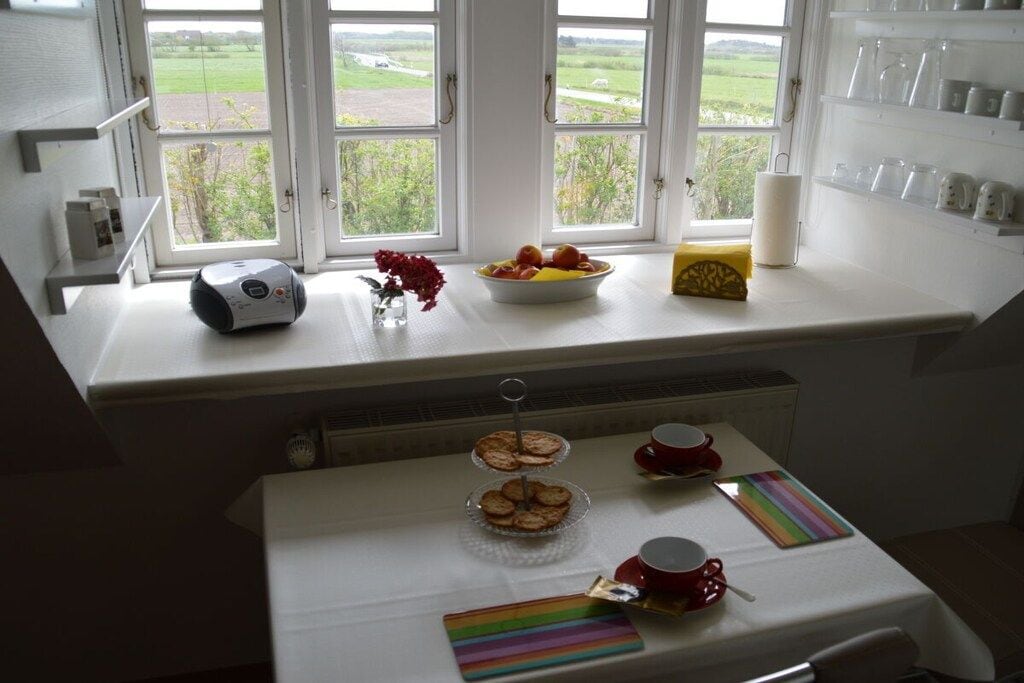 A breakfast setup with a table, a bowl of fruit, a candle, and a coffee station.