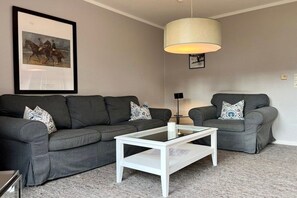 A living room with a grey sofa, a white coffee table, a lamp, and a framed picture on the wall. - Holiday home in Nieblum with swimming pool (Nieblum)