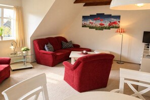 A red sofa set in a room with a white table, a floor lamp, and a painting of red flowers on the wall. - Haus Bornholm Holiday Apartment Anemone (Nieblum)