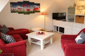 Un salon avec des canapés rouges, une table basse blanche, un téléviseur à écran plat et une lampe.
