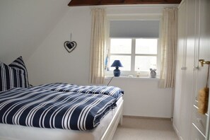 Une chambre à coucher avec un lit, une fenêtre avec des rideaux, une lampe et un objet décoratif en forme de cœur accroché au mur.
