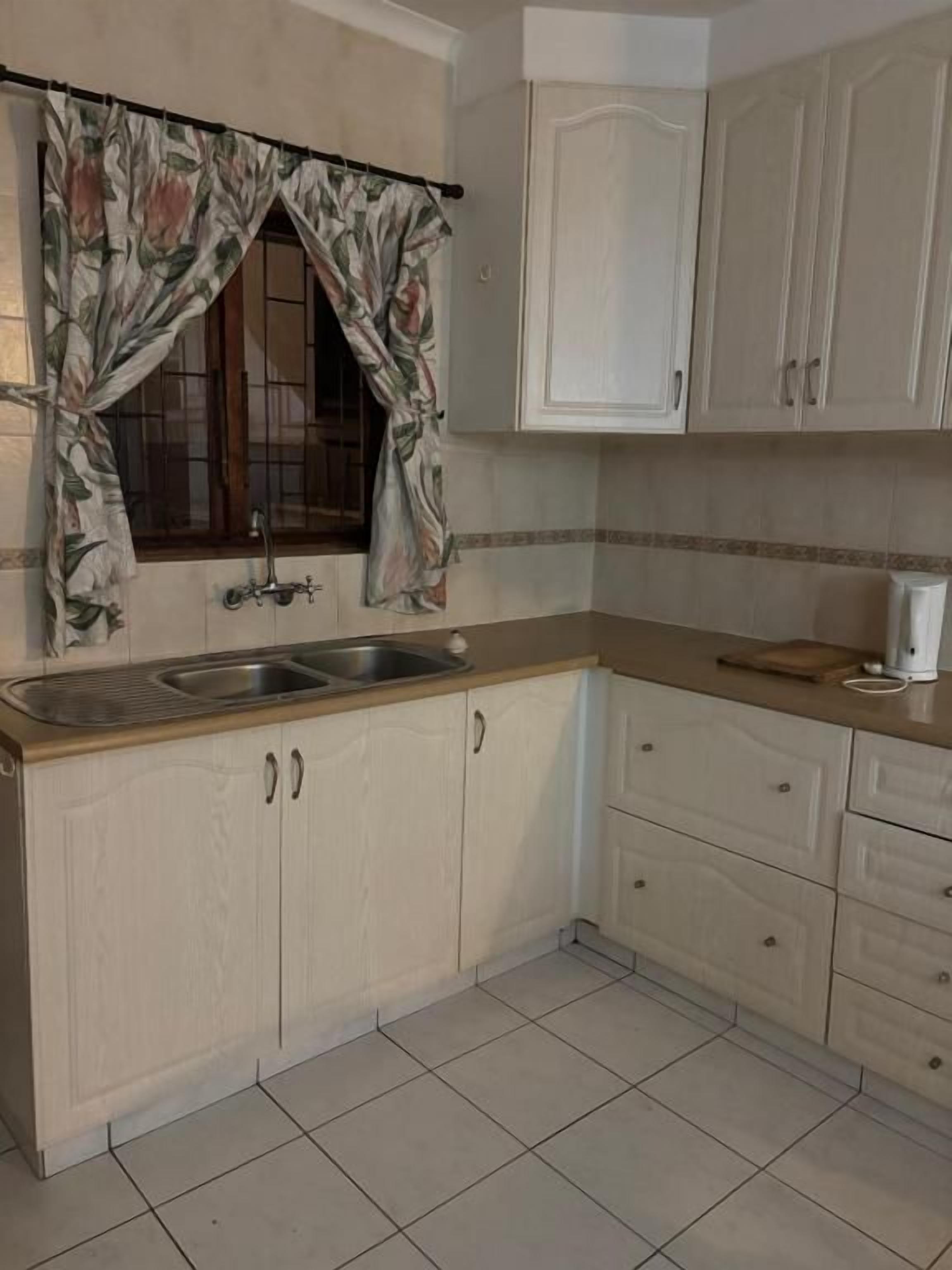 A kitchen with a double sink, white cabinets, a window with floral curtains, and a tiled floor.
