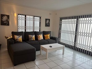 Una sala de estar con un sofá modular, una mesa de centro y ventanas amplias con barandillas de metal.