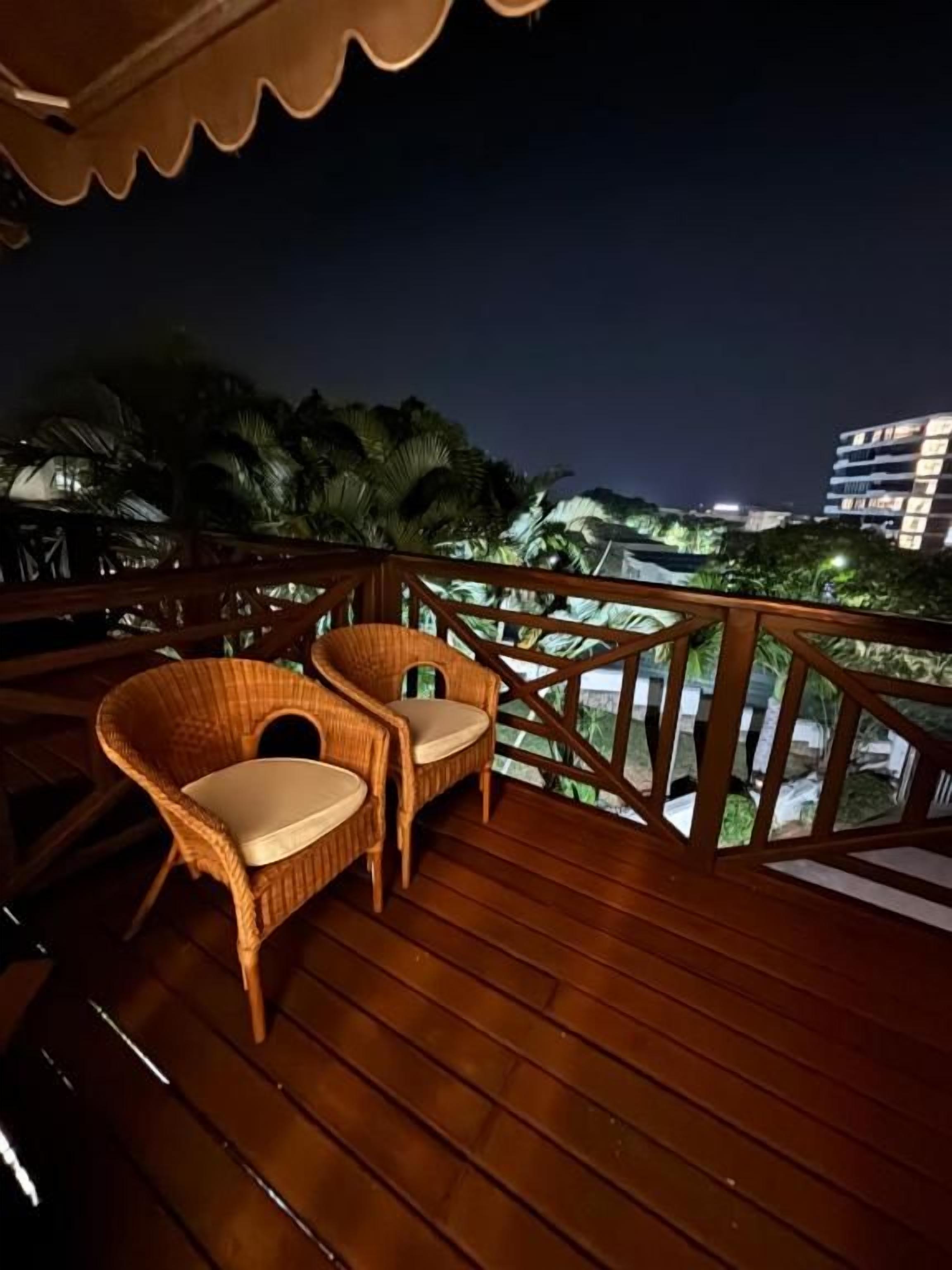 A wooden deck with wicker chairs and a railing overlooking a cityscape at night.