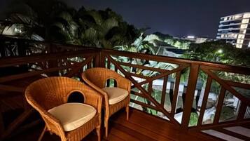 A wooden deck with wicker chairs and a railing overlooking a cityscape at night.