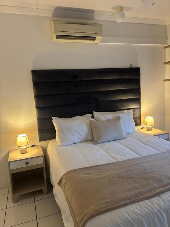 Una habitación de hotel con cama, lámparas de noche, mesita de noche y aire acondicionado.