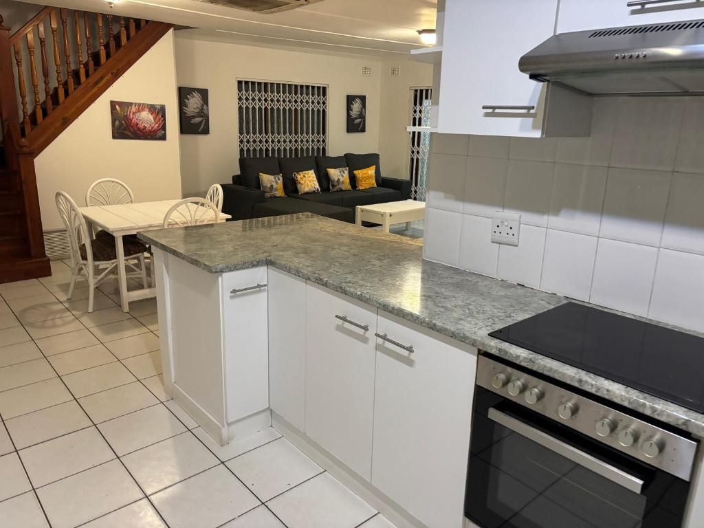 Une cuisine compacte avec des meubles blancs, une cuisinière encastrée et un coin repas comprenant une table et des chaises blanches.
