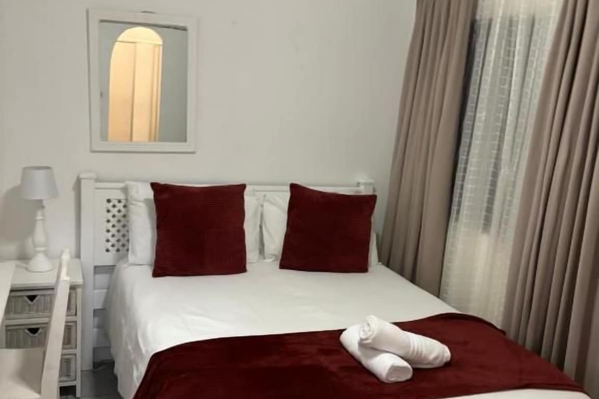 Ein Hotelzimmer mit Bett, Nachttisch, Lampe und einem Fenster mit Vorhängen.