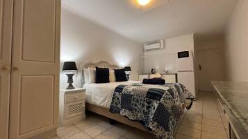 A bedroom with a bed, nightstands, a lamp, a dresser, and an air conditioning unit.