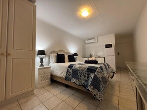 A bedroom with a bed, nightstands, a lamp, a dresser, and an air conditioning unit.