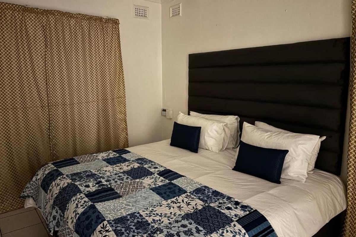 Ein Hotelzimmer mit Bett, Kopfteil und einem Fenster mit Vorhängen.