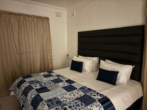 Habitación de hotel con cama, cabecera y ventana con cortinas.
