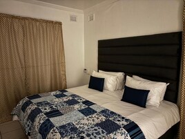Habitación de hotel con cama, cabecera y ventana con cortinas.
