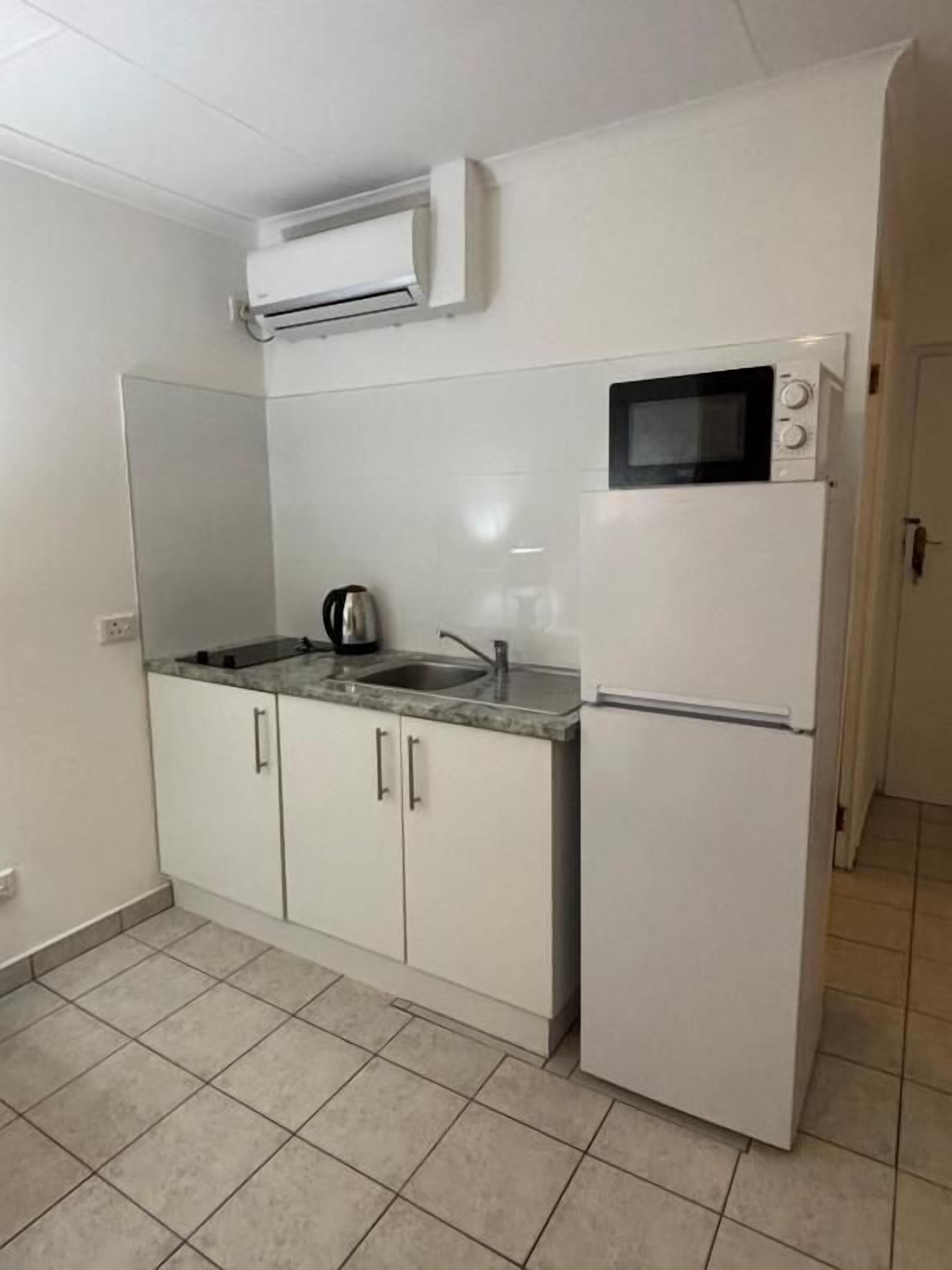 A compact kitchen with a microwave, sink, and a small refrigerator.