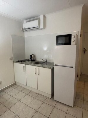 Una cocina compacta con microondas, pileta y un refrigerador pequeño.