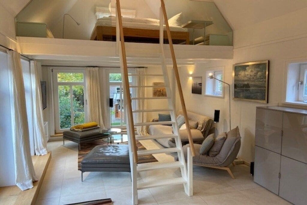 A modern interior with a loft bedroom, a sofa, a chair, and a ladder.