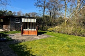 Un espace extérieur aménagé avec des sièges en bois, comprenant un banc et une table, entouré d’une pelouse bien entretenue et d’une clôture en bois.