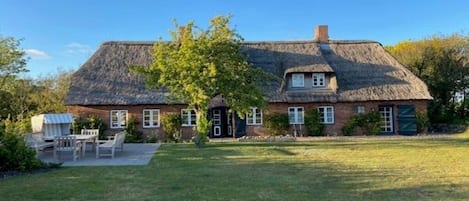 Ett tvåvåningshus med ett halmtak, en veranda och en liten trädgård.