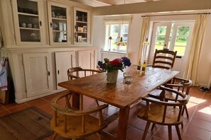 A dining area with a wooden table, four chairs, a cabinet with glass doors, and a window with curtains. - Holiday home in Nieblum with swimming pool (Nieblum)