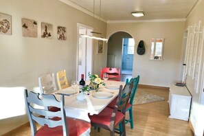 Un comedor con una mesa lista para cuatro personas, sillas, un refrigerador pequeño y una puerta que da a otra habitación.