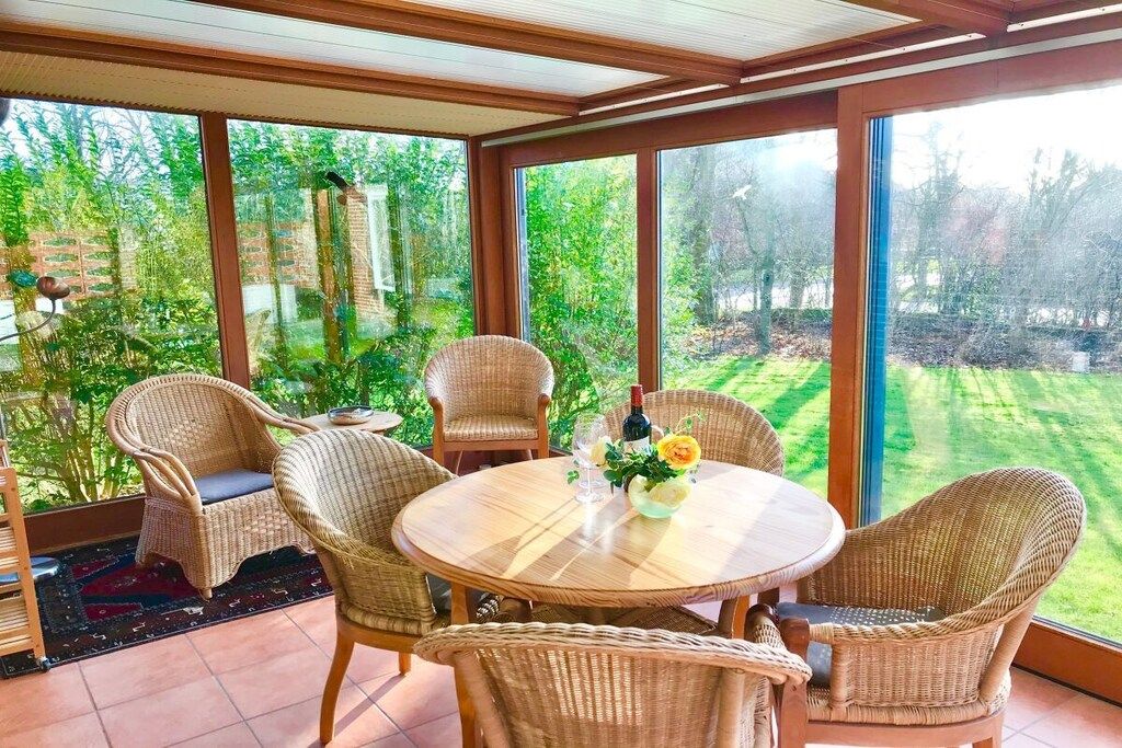 Une pièce baignée de lumière naturelle, avec une table ronde et des chaises en osier, de grandes fenêtres donnant sur un jardin.