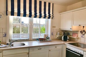Una cocina con gabinetes blancos, un lavamanos doble, una estufa y un ventanal con un cortinero a rayas.