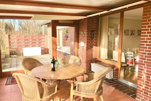 Eine überdachte Terrasse mit Korbmöbeln, einem Tisch mit Flasche und Glas sowie einer Backsteinwand.