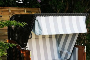 A wicker chair with a striped canopy, positioned outdoors with greenery in the background. - Haus Heike - Holiday Apartment 1st Floor (Utersum)