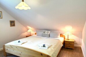 Ein Schlafzimmer mit schrägen Wänden, einem Bett mit Holzrahmen, zwei Nachttischlampen und einem Kissen mit einer Nummer.